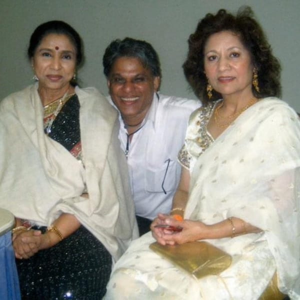 Three people, two women in saris and a man in a white shirt, smiling at the camera.