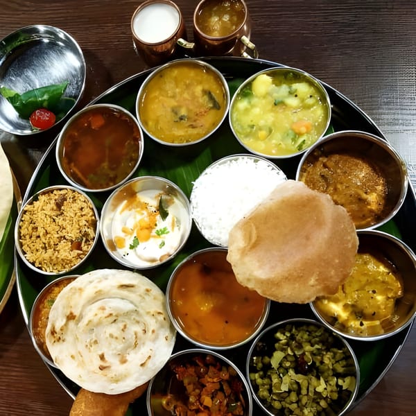 A vibrant South Indian thali meal with various curries, rice, bread, and drinks on a banana leaf.