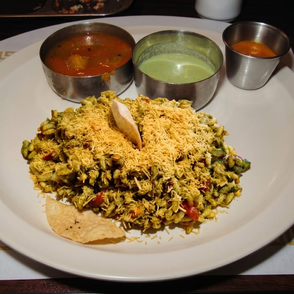 A plate of green Poha with sev, a papad, and three small bowls of sauces.