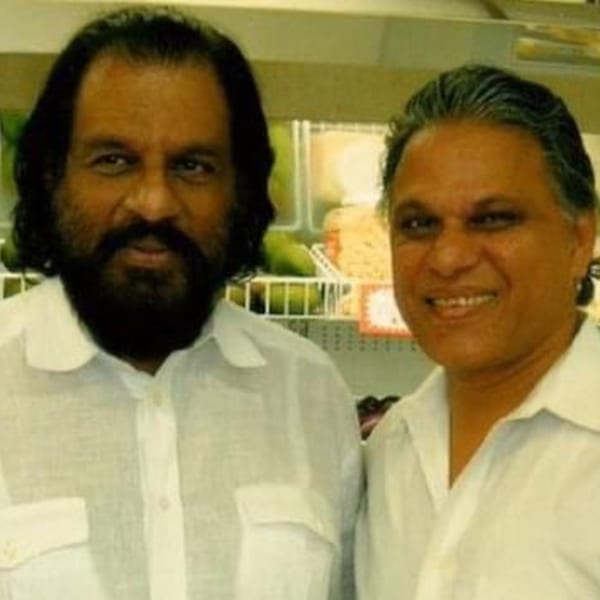 Two men in white shirts smile at the camera, with produce in the background.