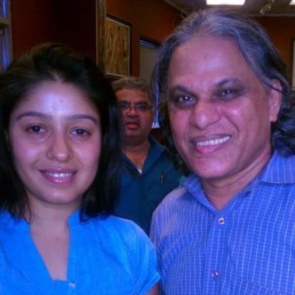 Two people smiling at the camera, with a third person blurred in the background.