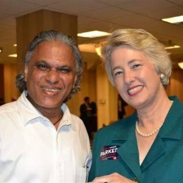 A man with long gray hair and a woman in a green jacket smiling at the camera.