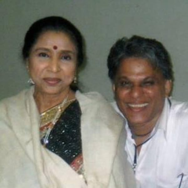 Asha Bhosle and a man smiling, with her wearing a sari and him a white shirt.
