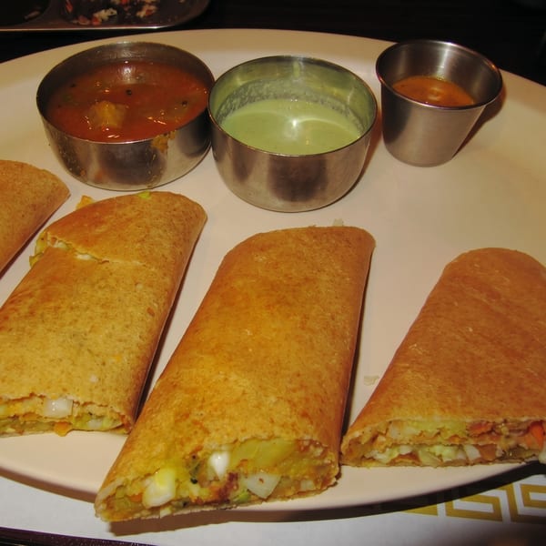 Three golden-brown dosas filled with vegetables and served with three small bowls of sauces.