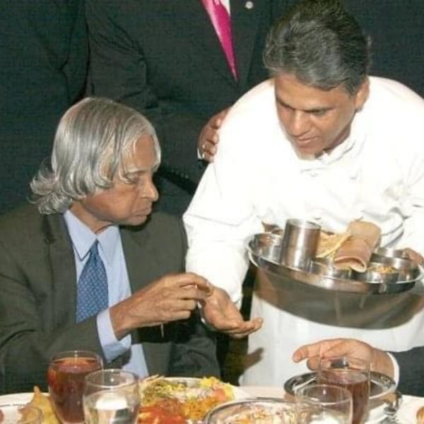 A server in a white uniform offers a tray of food to a man in a suit.