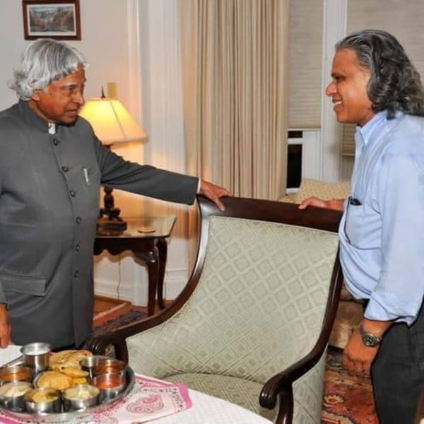 Two men, one with gray hair and one with long dark hair, conversing in a room with a tray of food.
