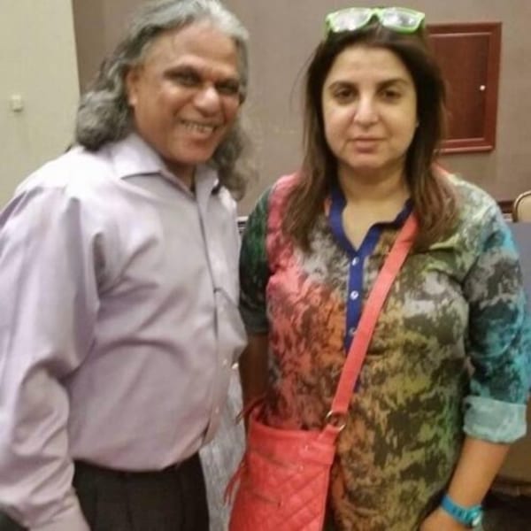 A man with long gray hair and a woman with a colorful shirt pose together, smiling.