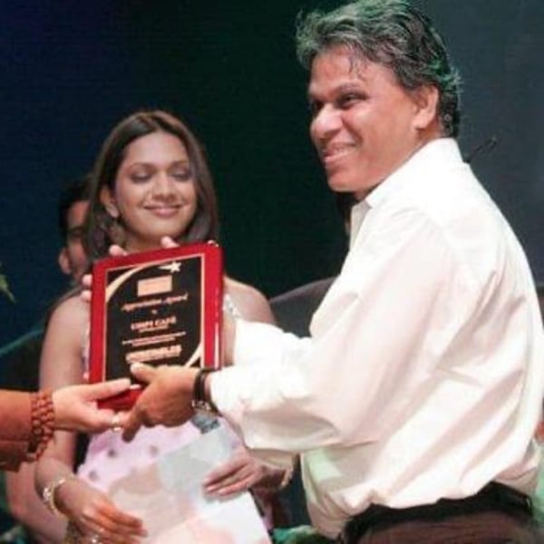 A man in a white shirt receives a red and black plaque from another person.