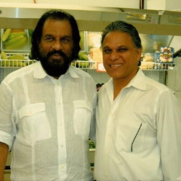 Two men in white shirts smile at the camera in front of a refrigerated display case.