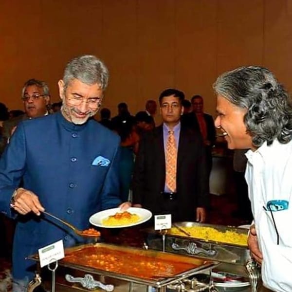 Two men at a buffet, one serving himself from a chafing dish of Indian food.