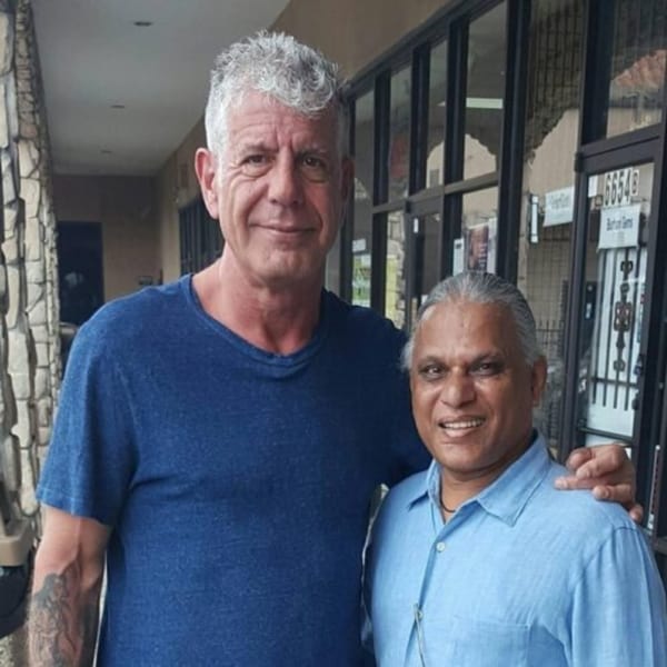 Anthony Bourdain with his arm around a smiling man in a light blue shirt.
