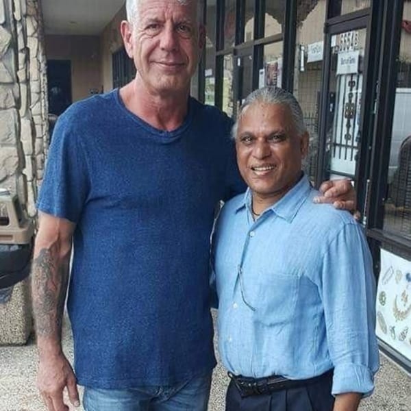 Anthony Bourdain and a man in a light blue shirt smiling with arms around each other.